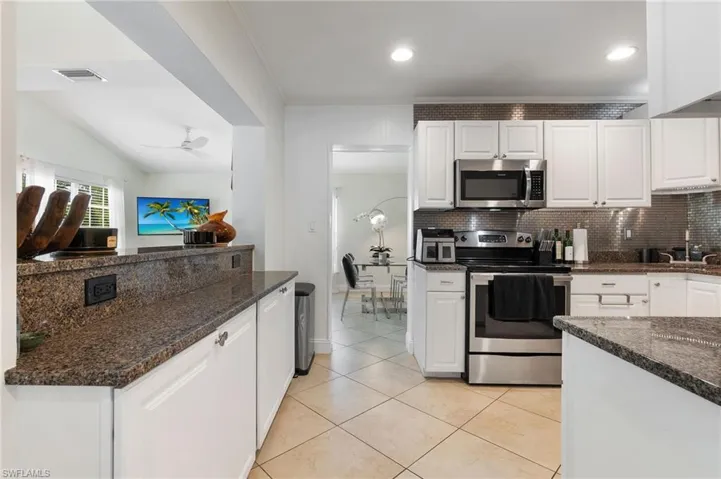 Kitchen with white cabinetry, appliances with stainless steel finishes, dark stone counters, tasteful backsplash, and crown molding
