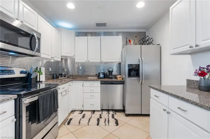 Kitchen with stainless steel appliances, white cabinetry, dark stone countertops, light tile patterned floors, and backsplash