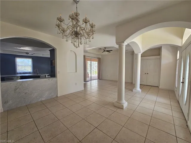 Unfurnished living room with a wealth of natural light, ornate columns, light tile floors, and ceiling fan with notable chandelier