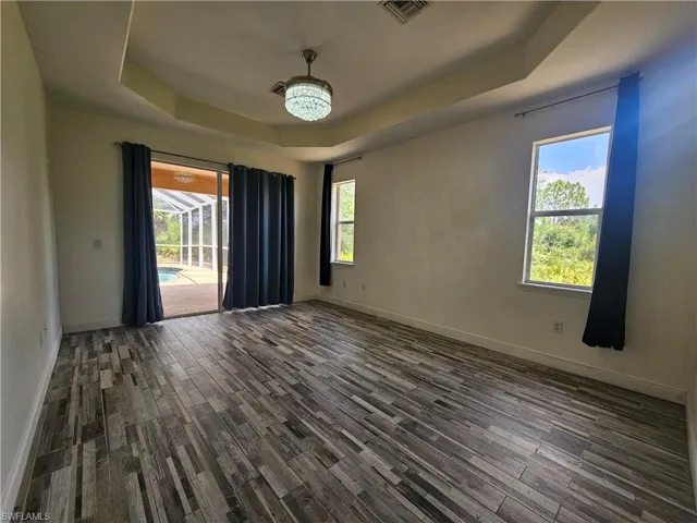 Empty room with a raised ceiling, an inviting chandelier, and dark wood-type flooring