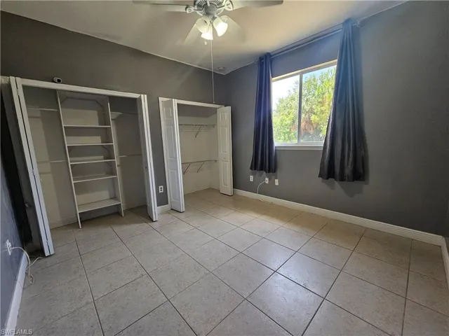 Unfurnished bedroom featuring ceiling fan, multiple closets, and light tile floors