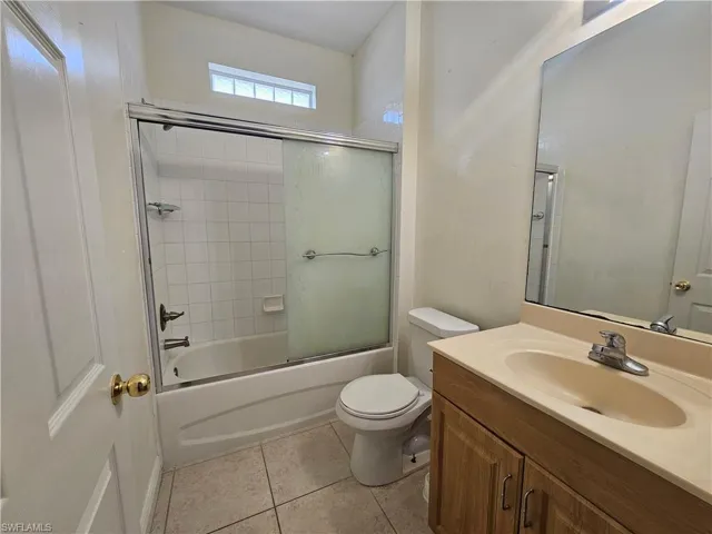 Full bathroom featuring shower / bath combination with glass door, tile flooring, oversized vanity, and toilet