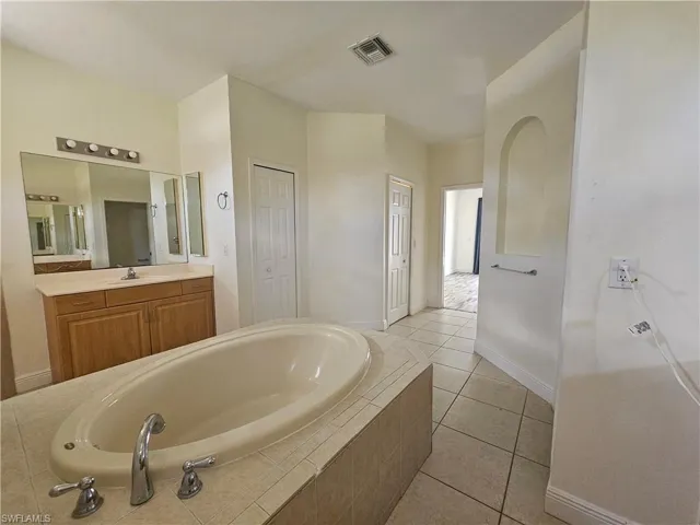Bathroom featuring vanity with extensive cabinet space, tiled tub, and tile floors