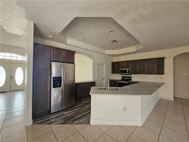 Kitchen featuring kitchen peninsula, stainless steel appliances, a tray ceiling, dark brown cabinets, and sink