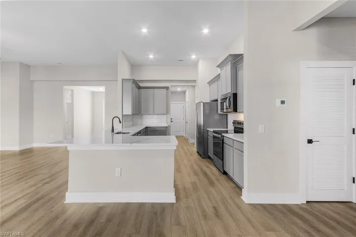 Kitchen with gray cabinetry, backsplash, stainless steel appliances, light wood-style flooring, and recessed lighting