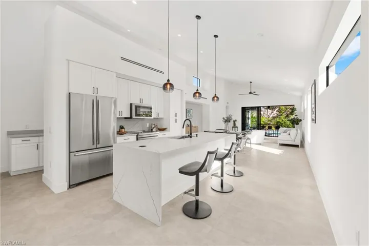 Kitchen featuring high vaulted ceiling, appliances with stainless steel finishes, a center island with sink, and white cabinets