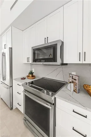 Kitchen featuring stainless steel appliances, white cabinetry, decorative backsplash, and light stone counters