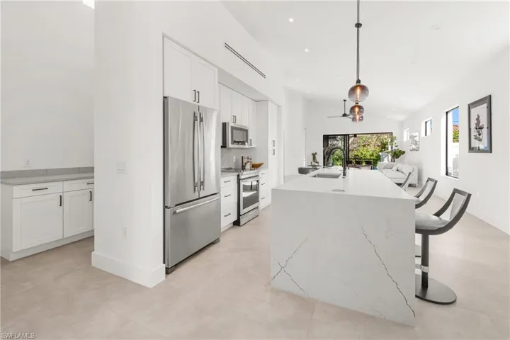 Kitchen featuring white cabinets, appliances with stainless steel finishes, open floor plan, a kitchen island with sink, and a sink
