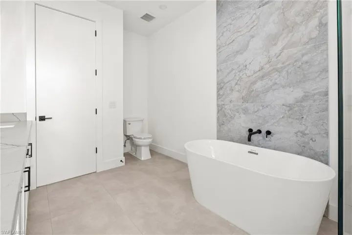 Full bathroom featuring a soaking tub, visible vents, tile walls, and toilet