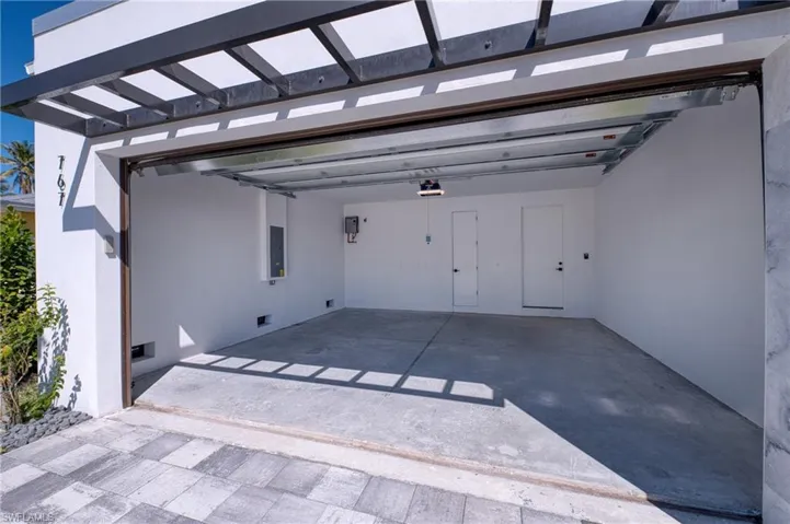 Garage with a garage door opener, electric panel, and driveway
