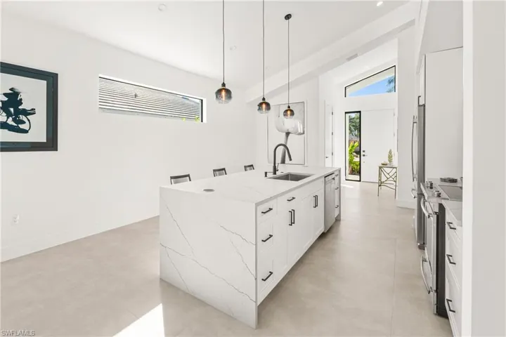 Kitchen featuring a center island with sink, white cabinets, stainless steel range oven, pendant lighting, and a sink
