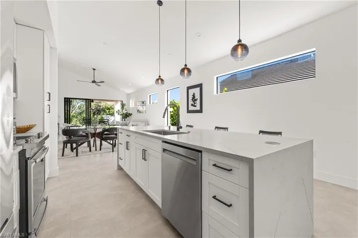 Kitchen featuring open floor plan, light stone countertops, stainless steel appliances, white cabinetry, and a sink