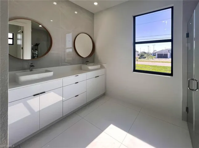 Bathroom featuring a shower with shower door, double sink vanity, and tile patterned flooring