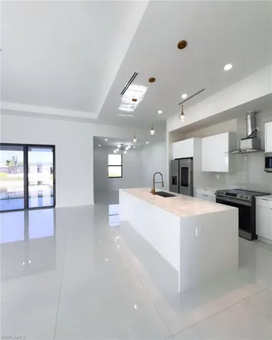 Kitchen with light tile patterned floors, wall chimney range hood, an island with sink, appliances with stainless steel finishes, and pendant lighting