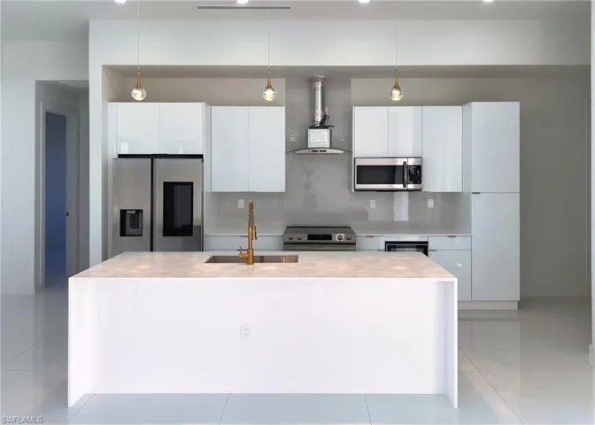 Kitchen featuring decorative backsplash, pendant lighting, wall chimney exhaust hood, a center island with sink, and appliances with stainless steel finishes