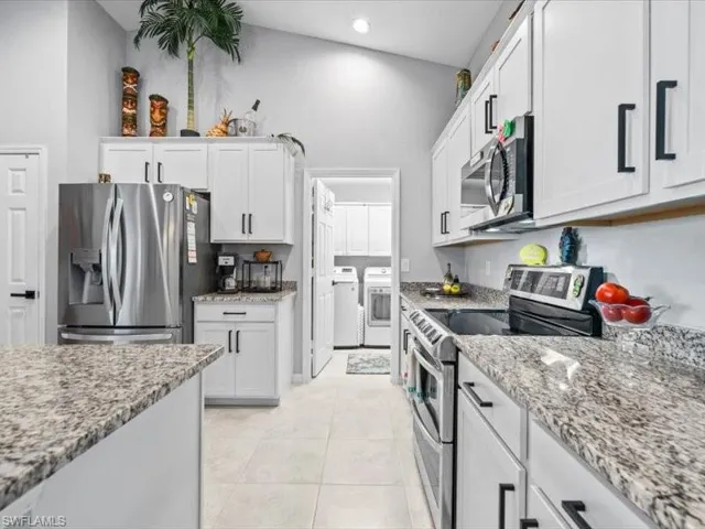 Kitchen with stainless steel appliances, a high ceiling, light stone counters, white cabinets, and washing machine and clothes dryer