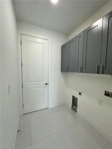 Clothes washing area with cabinets, hookup for an electric dryer, light tile floors, and washer hookup