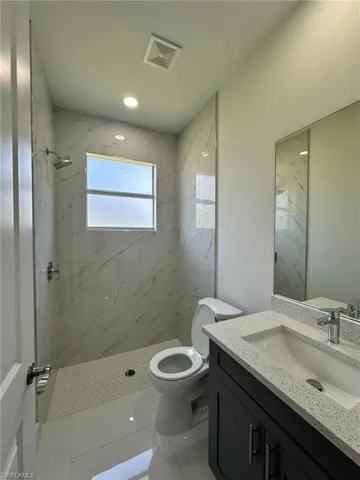 Bathroom featuring tile flooring, tiled shower, toilet, and large vanity
