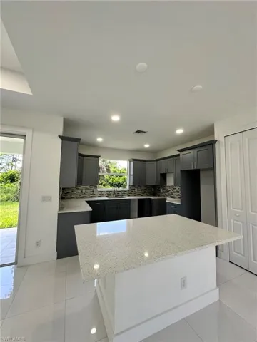 Kitchen featuring a kitchen island, light stone counters, backsplash, a kitchen bar, and light tile floors