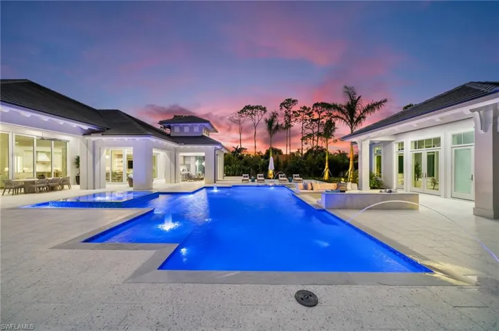 Pool at dusk featuring a patio, an in ground hot tub, pool water feature, and french doors