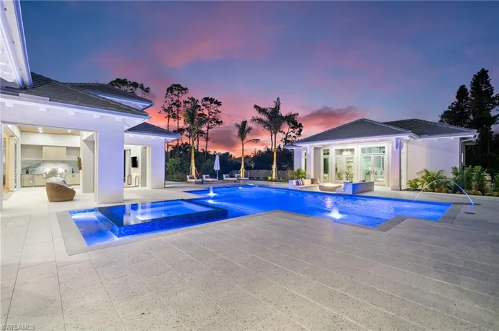 Pool at dusk featuring a patio, exterior kitchen, pool water feature, and an in ground hot tub