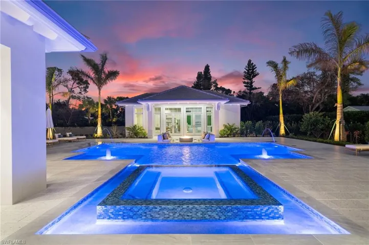 Pool at dusk featuring an in ground hot tub, a patio, and multiple pool water features