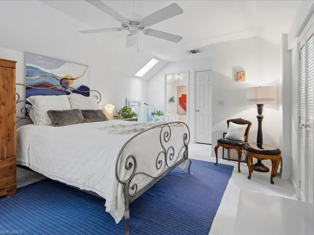 Vaulted ceiling room featuring white-painted wood flooring, a ceiling fan, and a skylight
