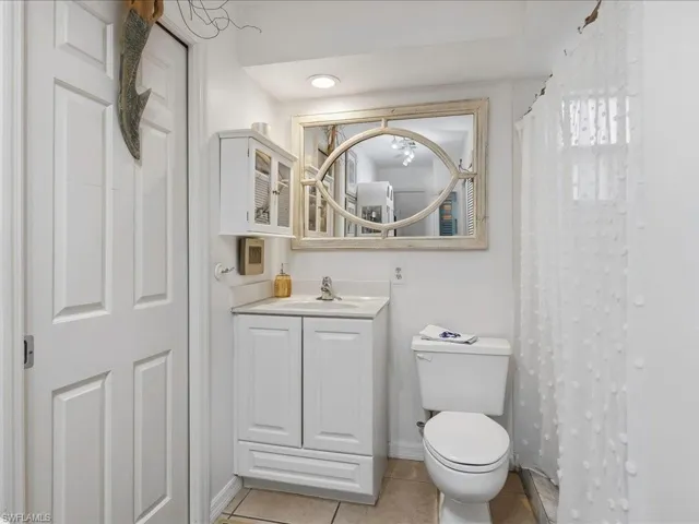 Bathroom featuring a white vanity with integrated sink, a built-in wall cabinet, a toilet, and tiled flooring
