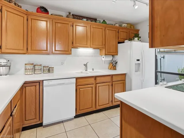 Kitchen featuring light wood cabinetry, white countertops, white subway tile backsplash, a double basin sink with a chrome faucet, and tile flooring