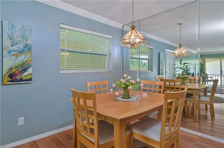 Bright dining space with crown molding, laminate wood flooring and a dramatic mirrored wall that reflects light and enhances the open feel of the room.