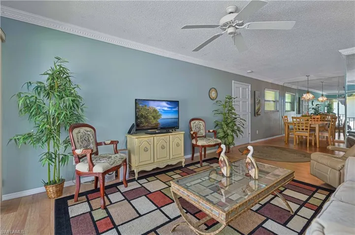 Spacious living area featuring attractive crown molding, laminate wood flooring and a ceiling fan, with an open flow into the dining area and plenty of natural light.