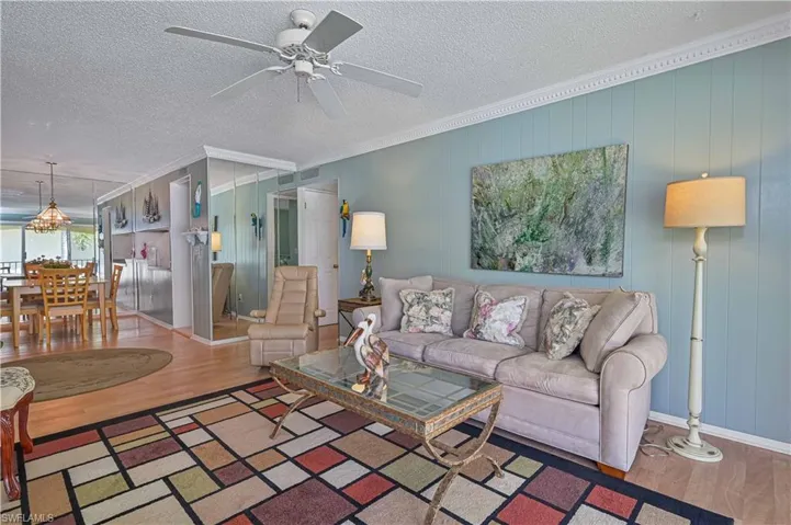 Another view highlights the spacious open-concept layout, ceiling to floor mirrors, crown molding, ceiling fan and laminate wood flooring, with an easy flow from the living room into the dining area.