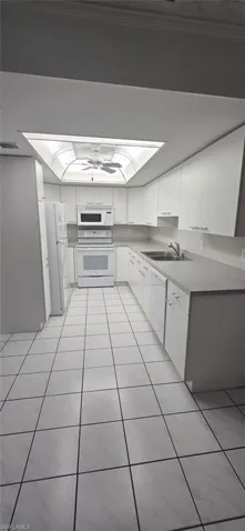 Kitchen featuring white appliances, white cabinetry, light tile patterned floors, and light countertops