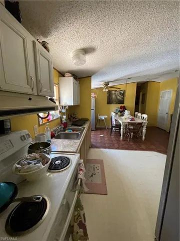 Kitchen featuring light hardwood / wood-style floors, exhaust hood, stove, sink, and a textured ceiling