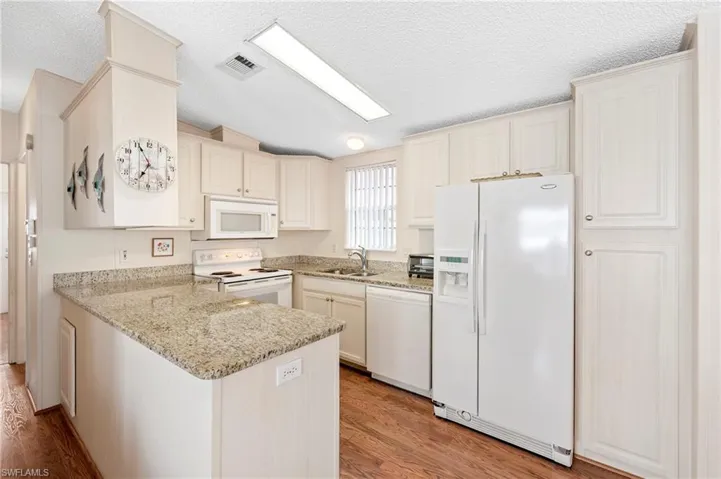 Kitchen with visible vents, light wood-style floors, a sink, white appliances, and a peninsula