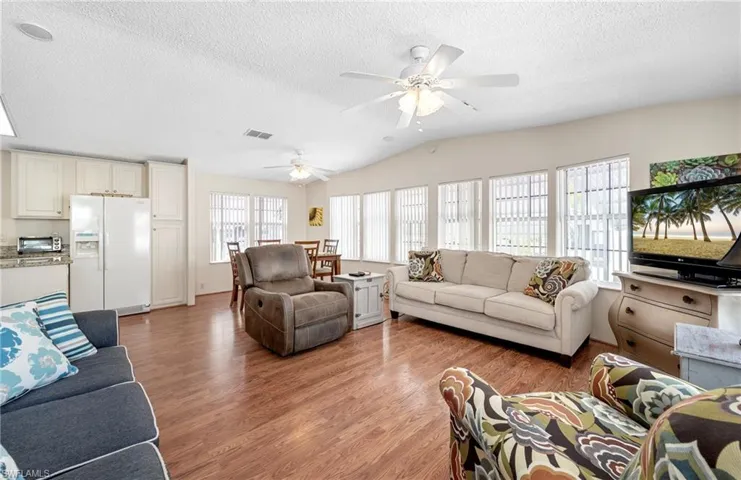 Living room with lofted ceiling, ceiling fan, a textured ceiling, visible vents, and light wood-type flooring