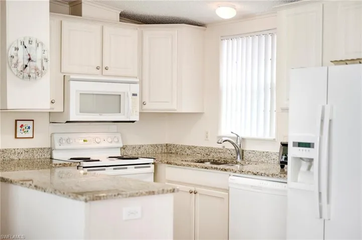 Kitchen featuring white appliances, a sink, light stone counters, and white cabinetry