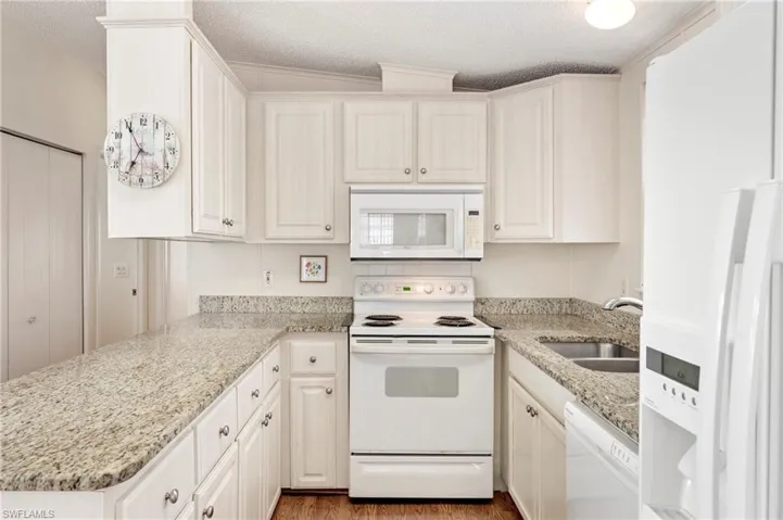 Kitchen featuring white appliances, white cabinetry, a sink, and a textured ceiling