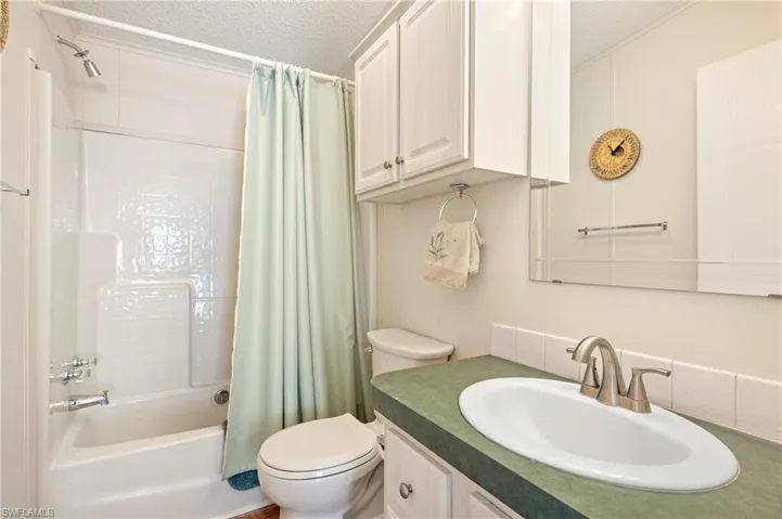 Bathroom featuring shower / bath combination with curtain, a textured ceiling, toilet, and vanity