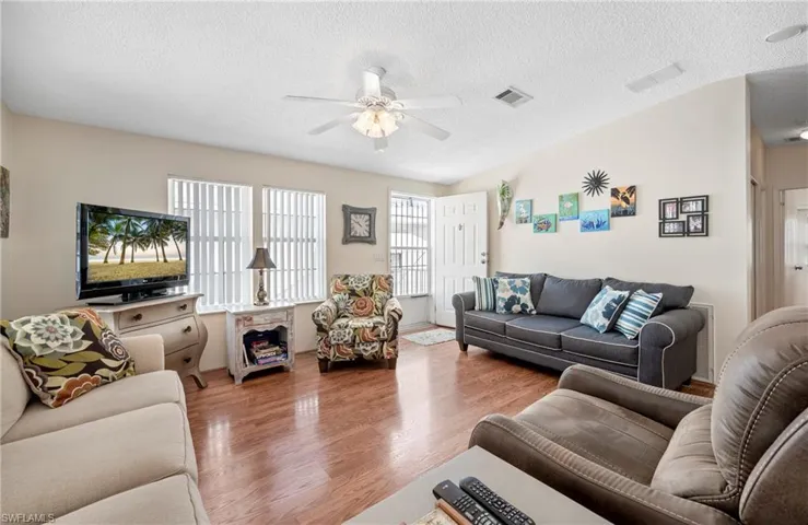 Living room featuring a textured ceiling, wood finished floors, visible vents, and a ceiling fan