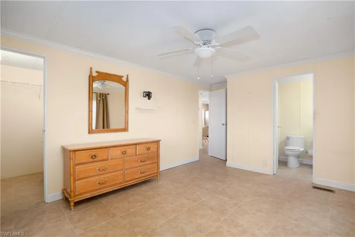 Bedroom featuring ensuite bath, ceiling fan, ornamental molding, a walk in closet, and a closet
