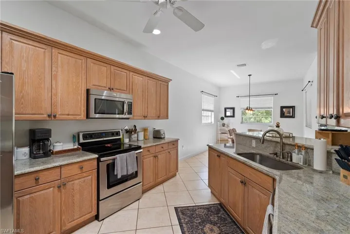 Kitchen featuring ceiling fan with notable chandelier, light stone countertops, appliances with stainless steel finishes, hanging light fixtures, and sink