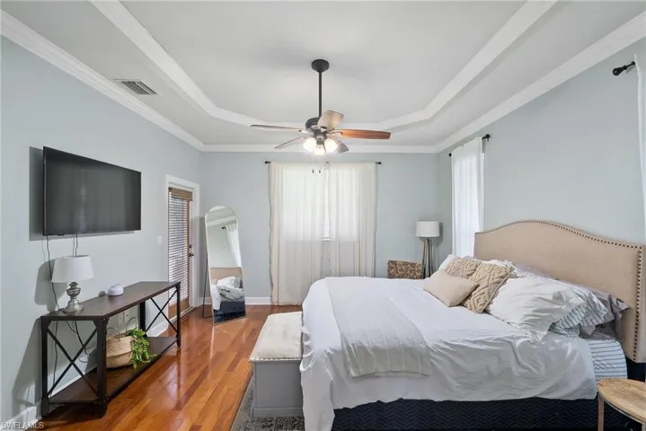 Bedroom featuring a tray ceiling, ceiling fan, crown molding, and wood-type flooring