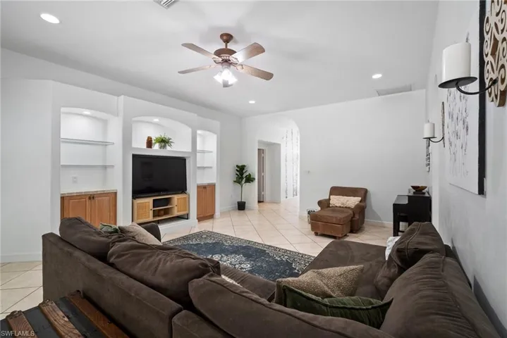 Living room with built in shelves, ceiling fan, and light tile patterned flooring