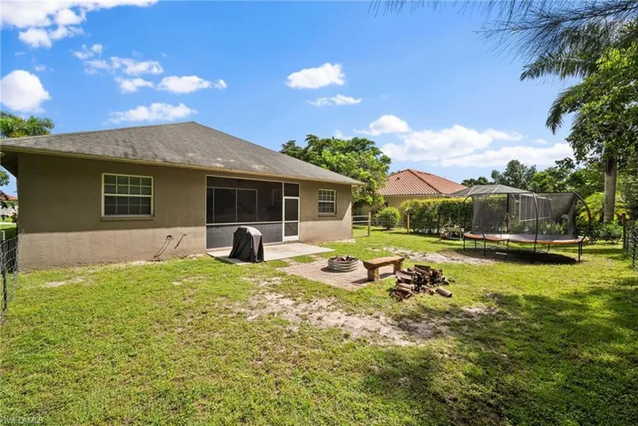 Rear view of house featuring an outdoor fire pit, a sunroom, a yard, and a trampoline