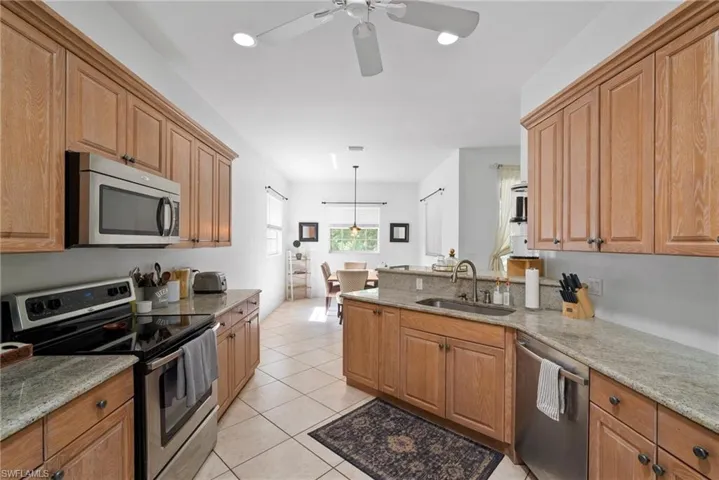 Kitchen featuring stainless steel appliances, sink, ceiling fan, light stone countertops, and a barn door