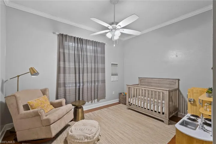 Bedroom with crown molding, a crib, wood-type flooring, and ceiling fan