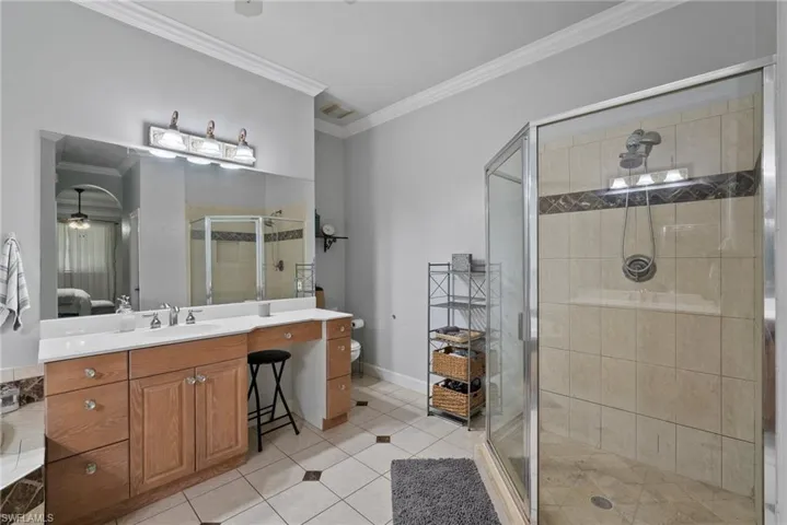 Bathroom featuring crown molding, toilet, a shower with shower door, ceiling fan, and vanity