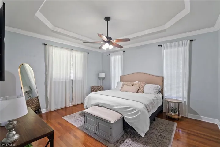 Bedroom with crown molding, a raised ceiling, ceiling fan, and dark hardwood / wood-style floors