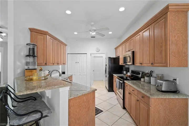 Kitchen featuring a kitchen breakfast bar, light stone countertops, ceiling fan, appliances with stainless steel finishes, and light tile patterned flooring